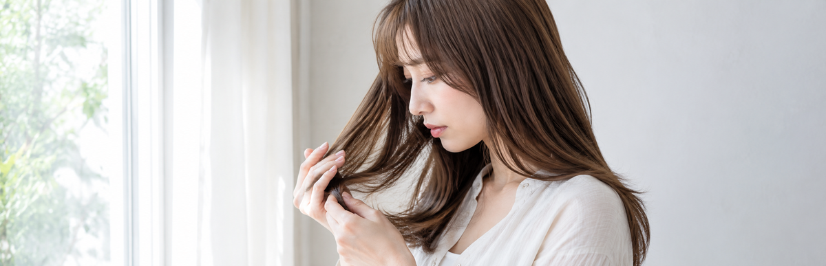 窓際で髪の色味を確かめる女性