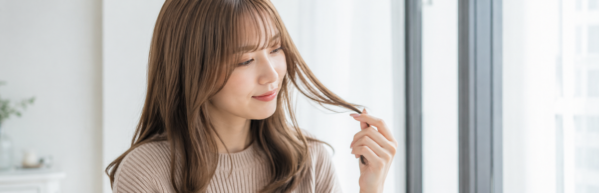 窓際で髪の色味を確かめる女性