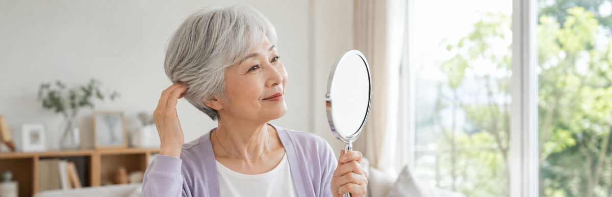 グレイヘアの女性が手鏡で白髪の色を確かめている様子