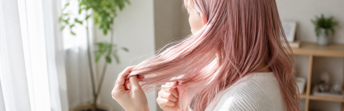明るく淡いパステルピンクの髪で毛先を確かめている様子