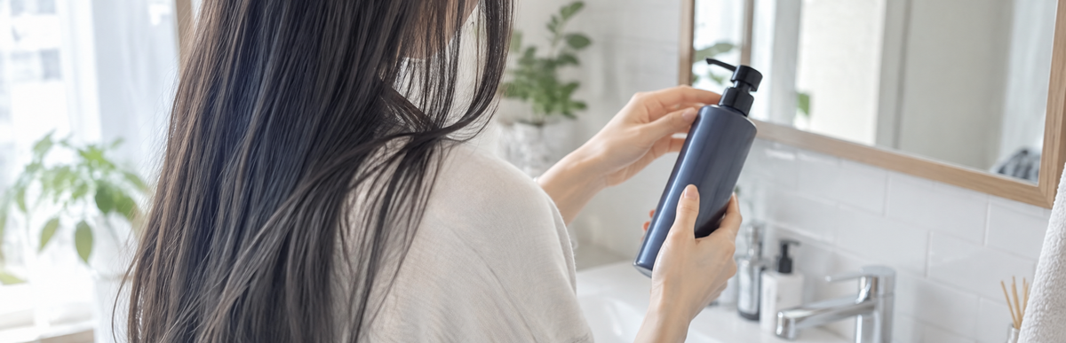 洗面所でカラーシャンプーのボトルを手に取る女性