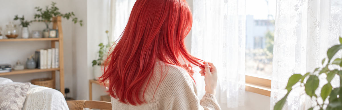 明るく鮮やかな赤の髪で毛先を確かめている様子