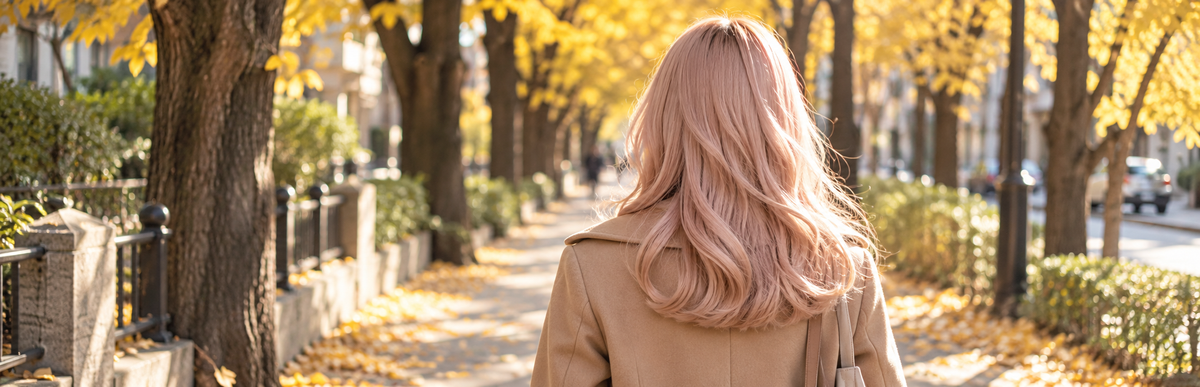 秋の並木道を歩く、ブリーチだけの金髪に淡いピンクをのせた髪の女性の後ろ姿