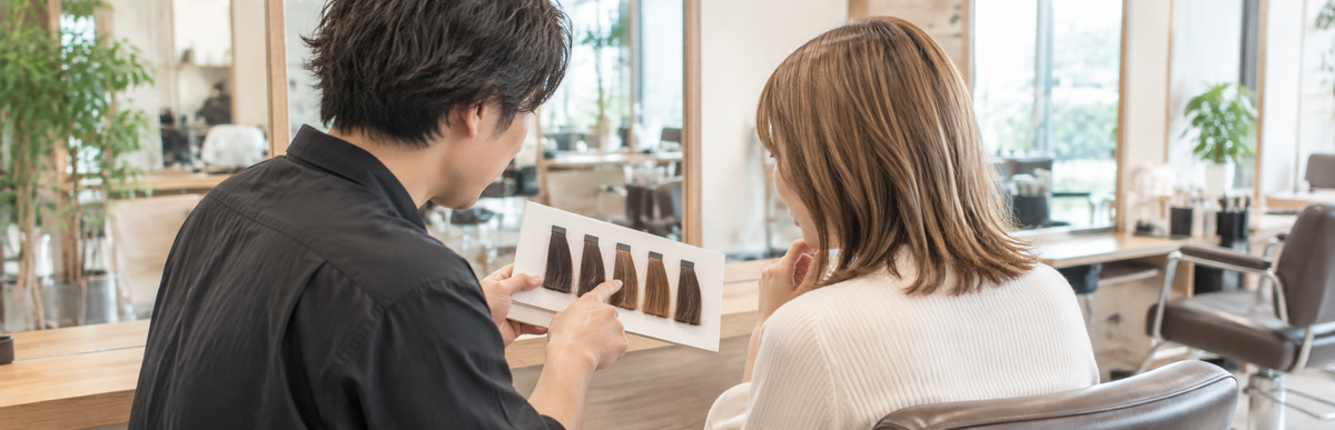 美容室のカウンセリングで美容師が見せる暗めのブラウンの毛束見本を見ている女性