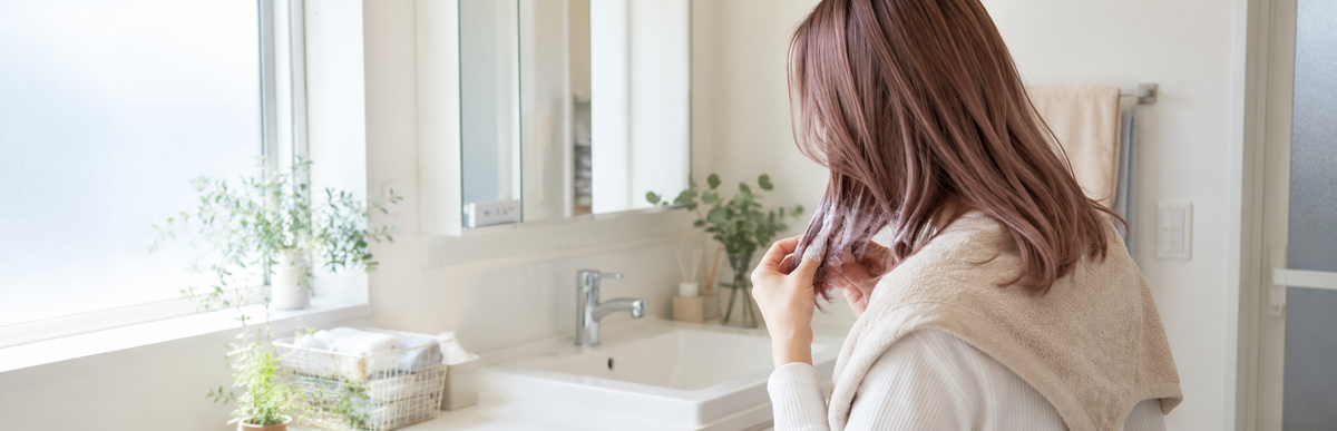 洗面所で肩にタオルをかけ、ピンクブラウンの髪の毛先にカラーシャンプーの泡をなじませる女性